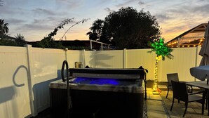Un jacuzzi en un patio trasero con una valla blanca, una mesa y sillas de patio.