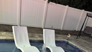 Una piscina con dos sillas reclinables blancas y un adorno pequeño en el borde.