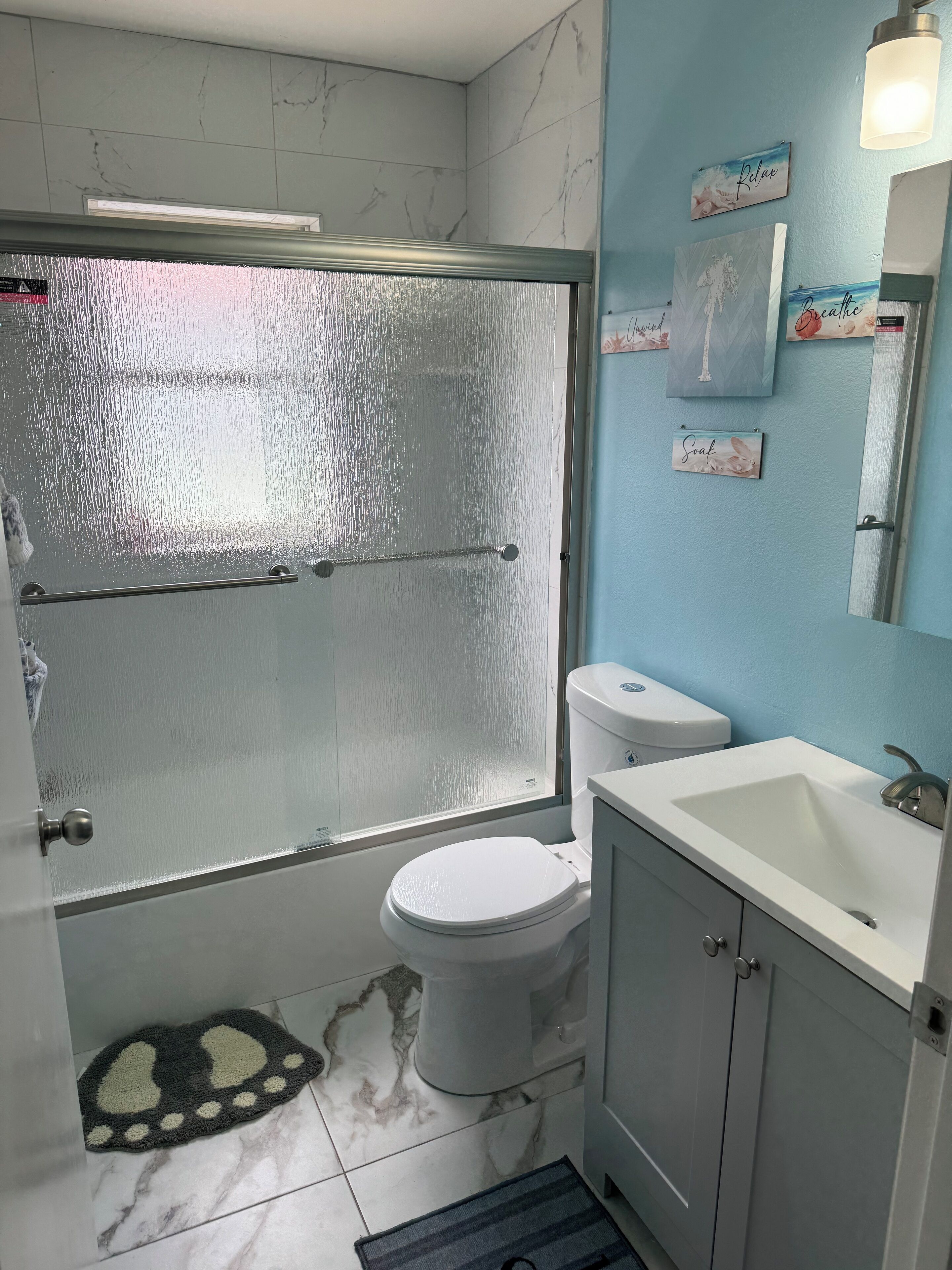 Un baño con cabina de ducha de vidrio, inodoro, lavamanos y espejo.