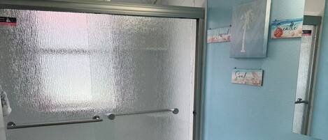 Un baño con cabina de ducha de vidrio, inodoro, lavamanos y espejo.