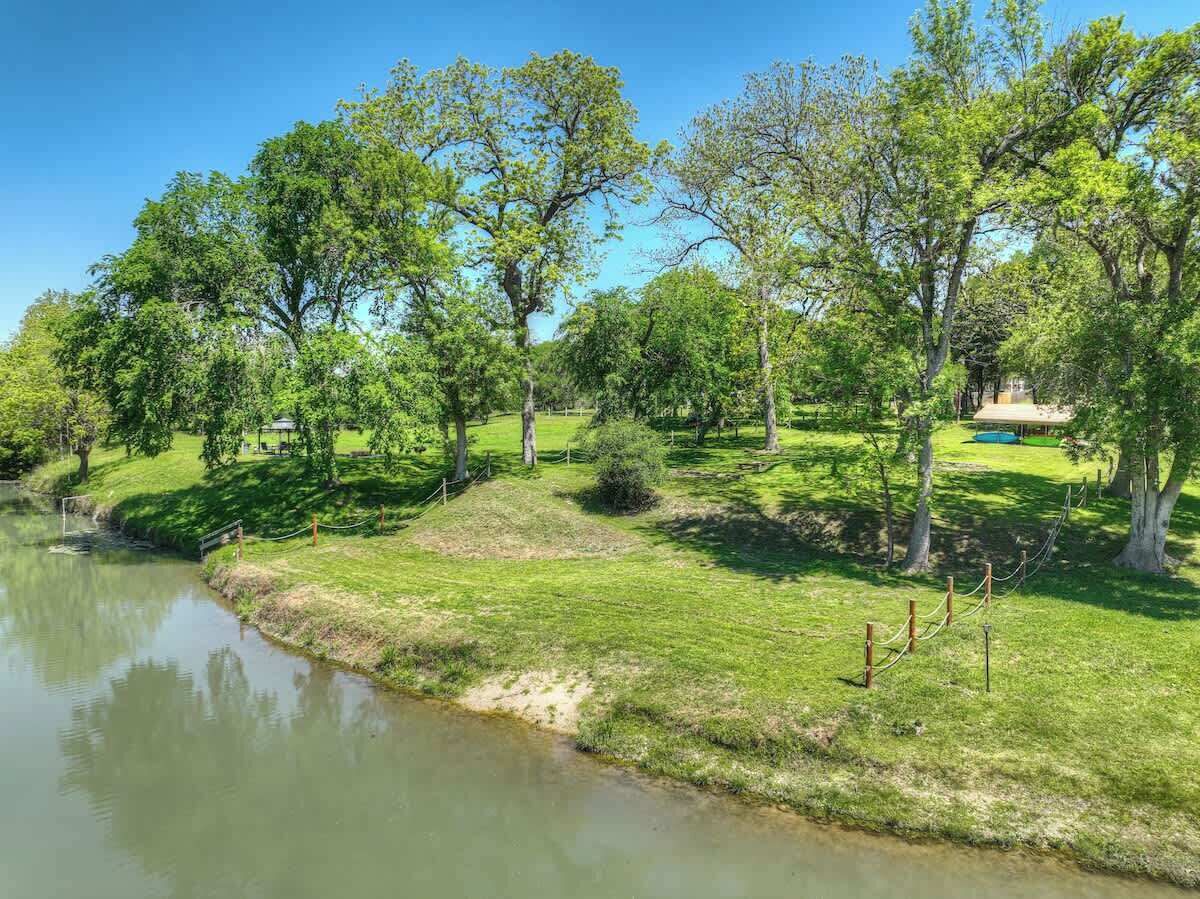 A serene riverside park with grassy areas, trees, and a small bridge.