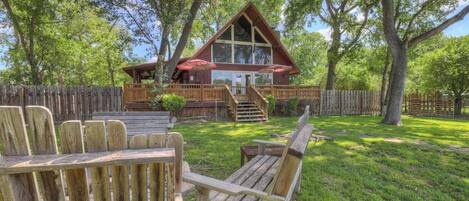 A wooden cabin with a deck, surrounded by trees.