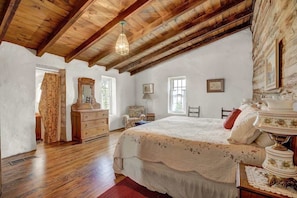 A bedroom with a wooden ceiling, a bed with a floral bedspread, a dresser, a mirror, and a window.