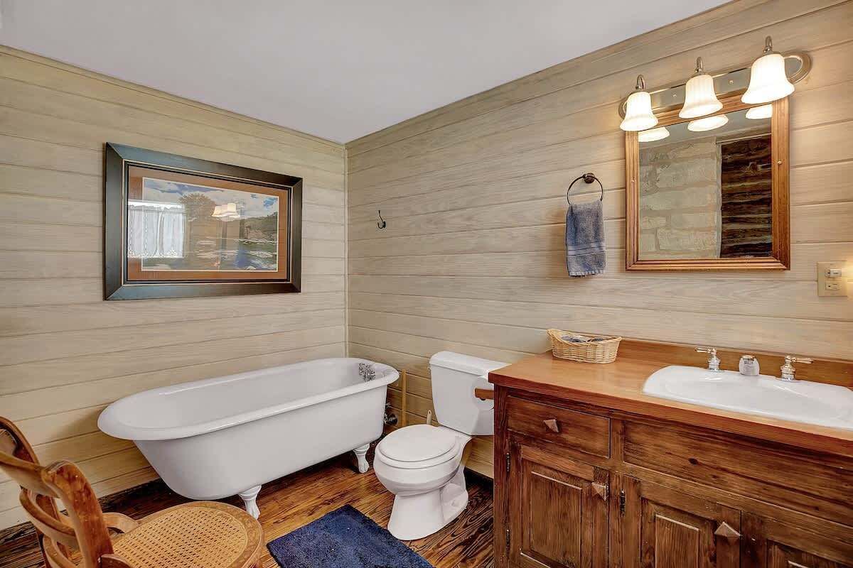 Een badkamer met een houten wand, een badkuip, een toilet, een wastafel en een spiegel.