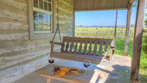A wooden bench with a picnic table, a bottle of wine, and a fruit platter. - Historic Log Cabin Retreat Near Town on 5 Acres! (Fredericksburg)