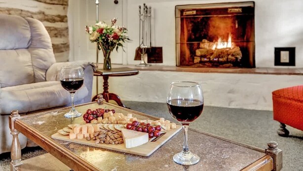 A cozy room with a fireplace, a sofa, a table with a cheese board and wine glasses. - Historic Log Cabin Retreat Near Town on 5 Acres! (Fredericksburg)