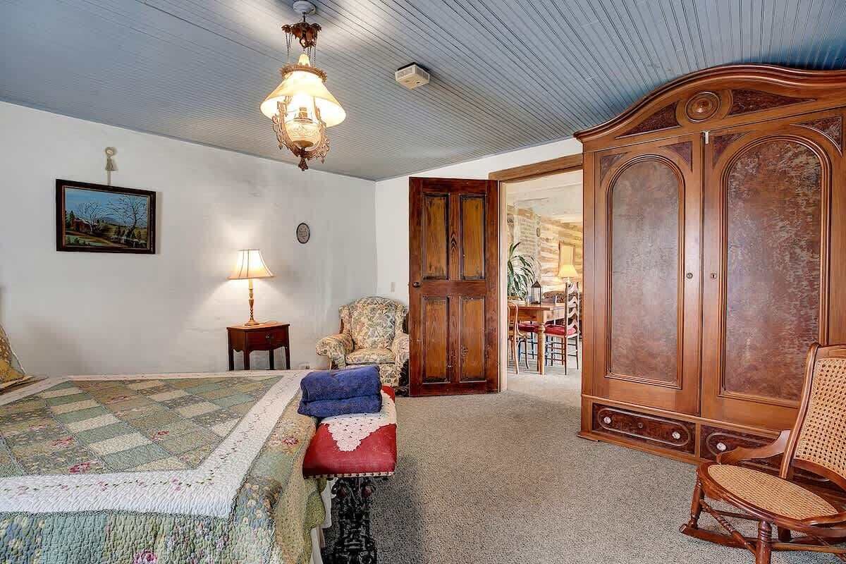 A room with a bed, a wooden wardrobe, a chair, a lamp, and a painting on the wall.