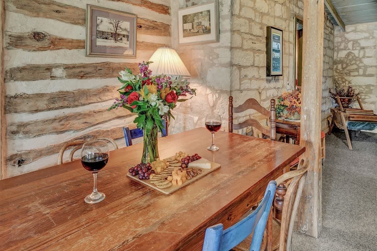 A rustic wooden table with a wine glass, cheese, and flowers.