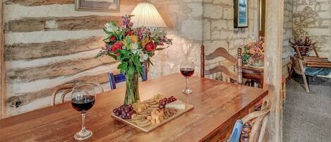 A rustic wooden table with a wine glass, cheese, and flowers.