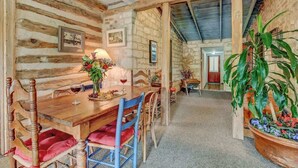 A rustic dining area with a wooden table, chairs, and a potted plant. - Historic Log Cabin Retreat Near Town on 5 Acres! (Fredericksburg)