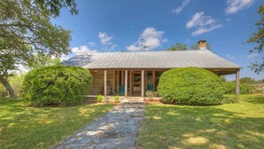 A log cabin with a stone pathway leading to the entrance, surrounded by well-maintained grass and bushes. - Historic Log Cabin Retreat Near Town on 5 Acres! (Fredericksburg)
