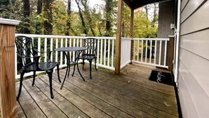 Una terraza de madera con baranda blanca, dos sillas de metal negro y una mesita.