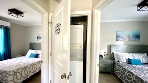 A hotel room with two beds, a wardrobe, a small table, and a painting on the wall.
