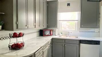 A kitchen with grey cabinets, a white countertop, a red microwave, a sink, and a dishwasher.