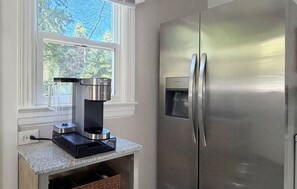 Una cocina con un refrigerador de acero inoxidable, una cafetera y una ventana con vistas a árboles.