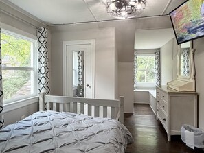 Ein Schlafzimmer mit Bett, Kommode, Fernseher und einem Fenster mit Vorhängen.