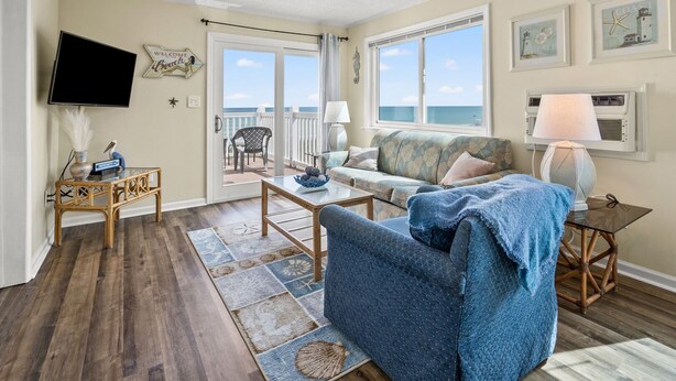 A living room with a view of the ocean, a television, and a balcony with outdoor furniture. - Amazing view from this 3rd story oceanfront condo w/private balcony and pool (North Myrtle Beach)