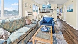 A spacious living room with a sofa, a coffee table, and a view of the kitchen and dining area. - Amazing view from this 3rd story oceanfront condo w/private balcony and pool (North Myrtle Beach)