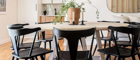 A modern dining area with a round table, black chairs, a woven pendant light, and a potted plant.
