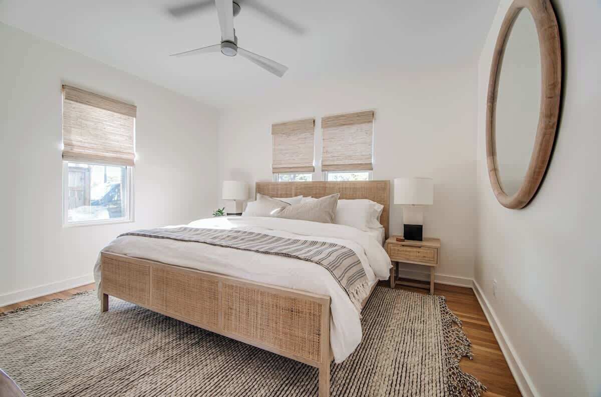 Un dormitorio con cama, mesitas de noche, ventilador de techo y un espejo grande.
