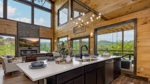 A modern kitchen with a large island, wooden walls, and large windows offering a view of the outdoors. - Peace Giver (Gatlinburg)