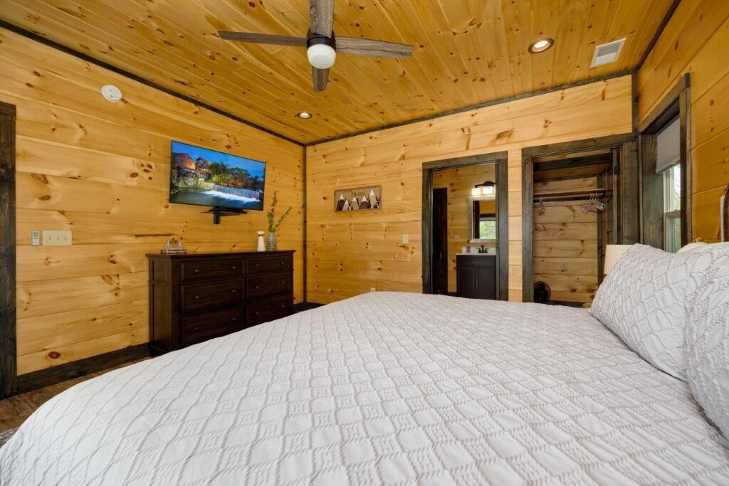 A wooden-paneled bedroom with a bed, dresser, and a television on the wall.