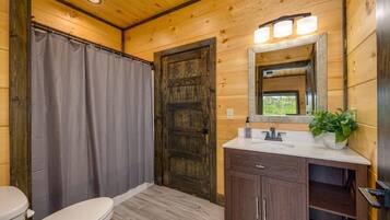 A wooden cabin bathroom with a toilet, a shower curtain, a wooden door, a sink with a mirror, and a potted plant.