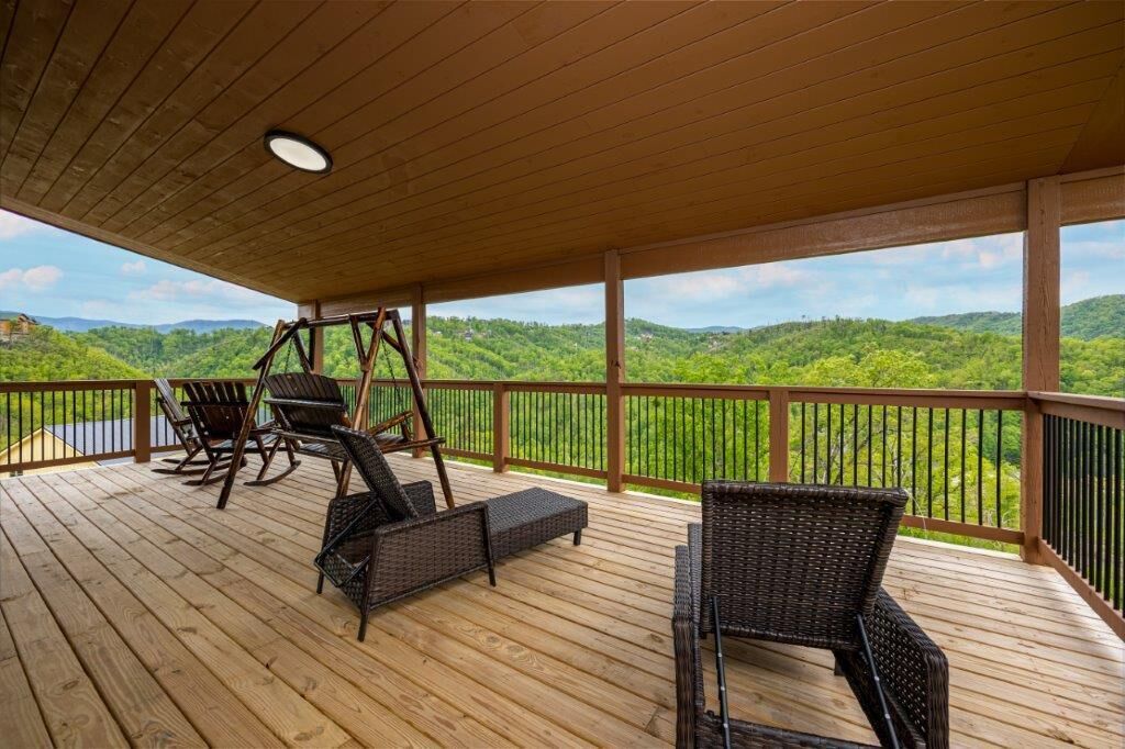 Eine Holzterrasse mit Korbmöbeln und einer Schaukel, mit Blick auf eine üppige, grüne Landschaft.