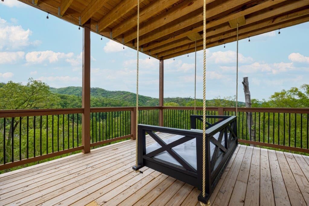 A wooden deck with a swing chair and a view of green hills.
