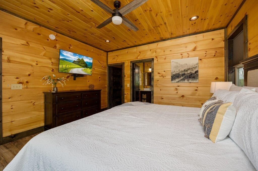 A wooden-paneled bedroom with a bed, a dresser, a television, and artwork on the walls.