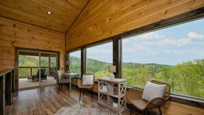 A wooden interior with large windows, a dining area, and a view of the forest. - Peace Giver (Gatlinburg)