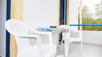 A balcony with two white plastic chairs and a small table with a checkered tablecloth.