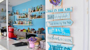 Un espace bar avec des étagères remplies de bouteilles et un panneau affichant des expressions comme « L’air est salé » et « Un nouveau siège pour se détendre ».