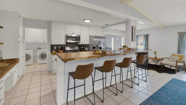 Uma cozinha moderna com armários brancos, bancada de madeira e uma ilha planejada com banquetas.