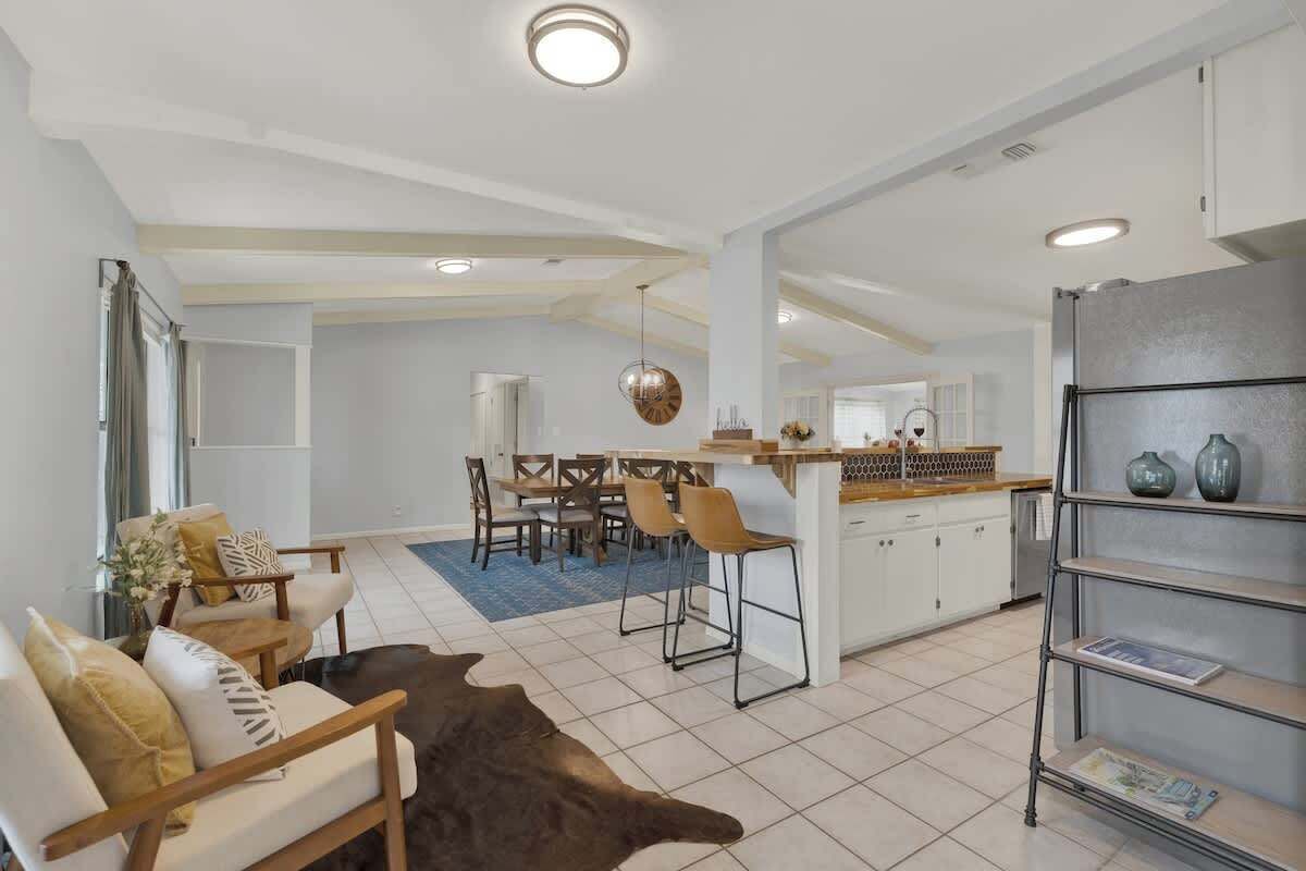 Una sala de estar moderna con un sofá, una mesa de centro y una alfombra. Hay un comedor con una mesa y sillas. La cocina cuenta con un refrigerador, estantes y una encimera.