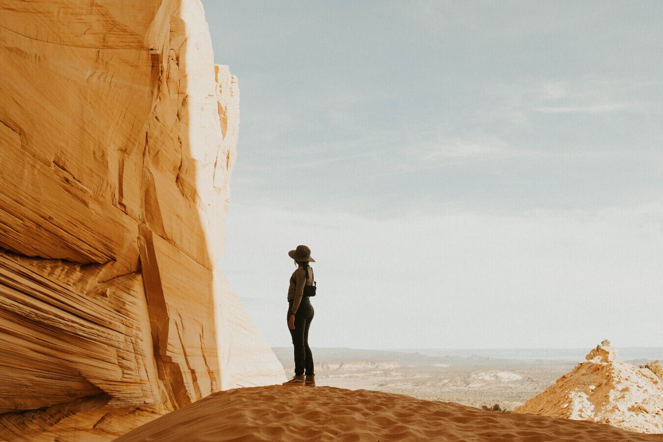 Une personne se tient sur une dune de sable, avec une grande formation rocheuse sur sa gauche.