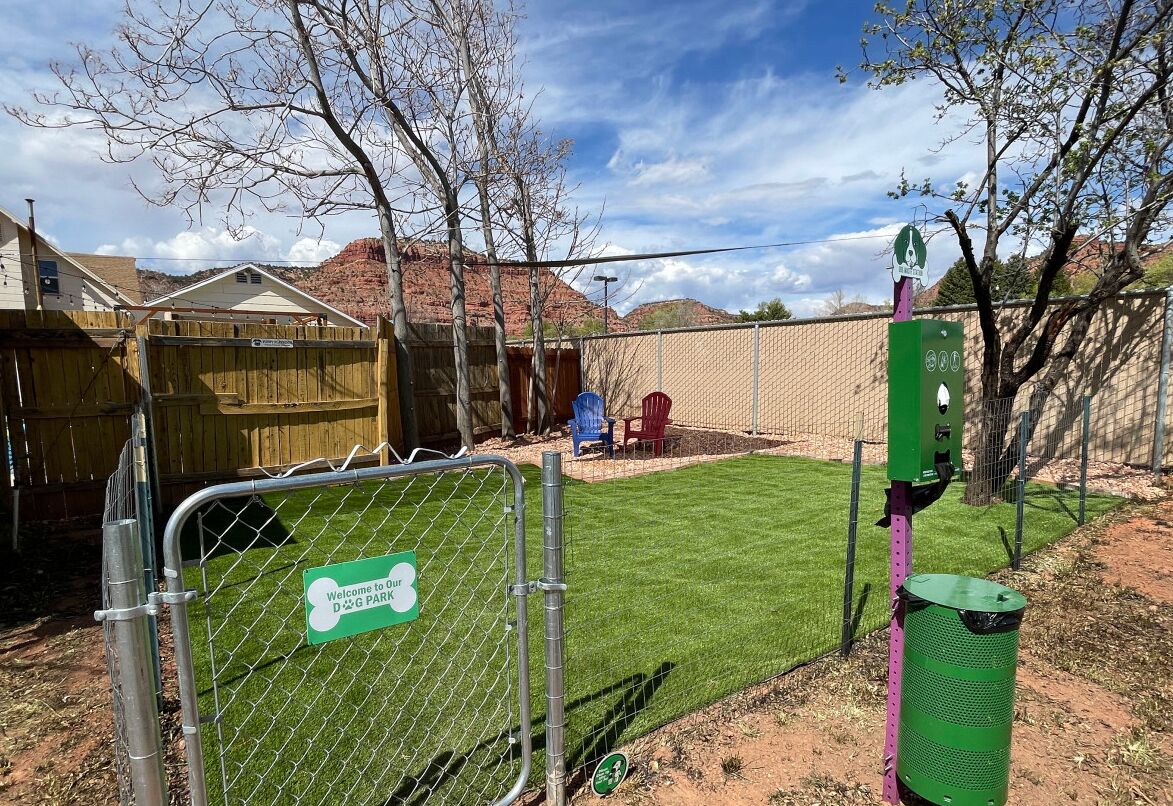 Un parc pour chiens clôturé, avec un panneau vert, une clôture en bois et une zone herbeuse.
