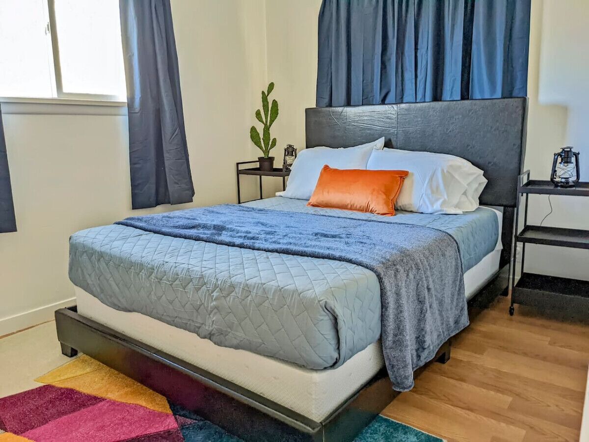 A bedroom with a bed, a nightstand, a potted plant, and a window with curtains.