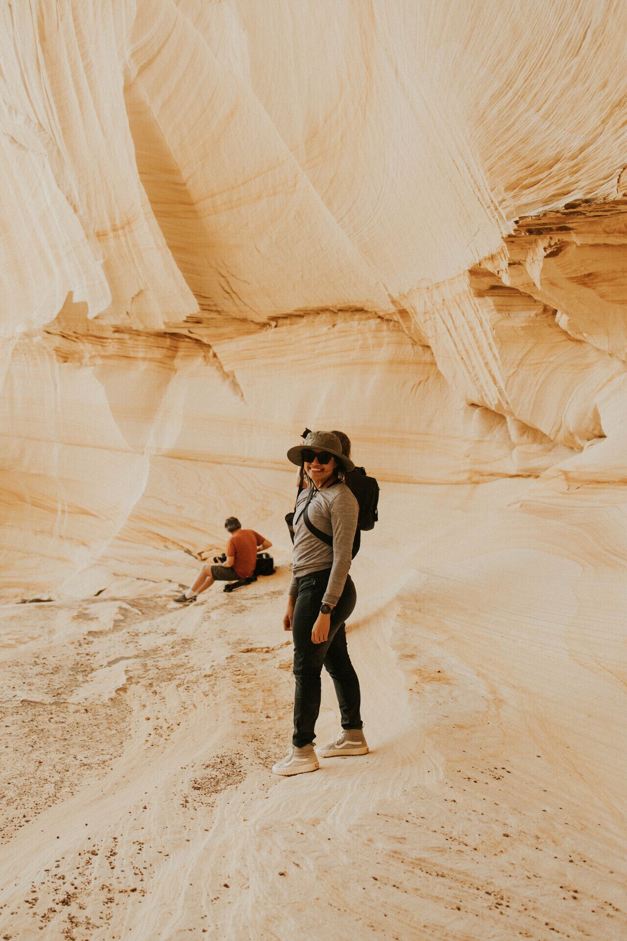 A person standing in a narrow canyon with a backpack, another person sitting in the background.