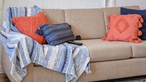En beige soffa med en randig pläd och två kuddar, en orange och en blå.