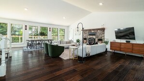 Een ruime woonkamer met een open haard, een eethoek en een televisie op een houten kast.