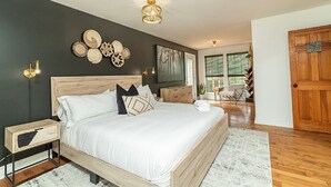 Een slaapkamer met een houten bed, nachtlampjes, een groot kunstwerk aan de muur en uitzicht op de kamer.