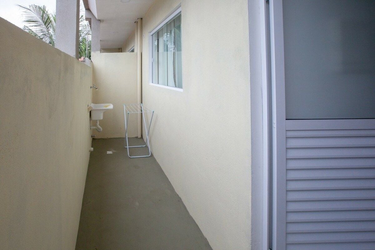 A narrow corridor with a white sink, a drying rack, and a window.