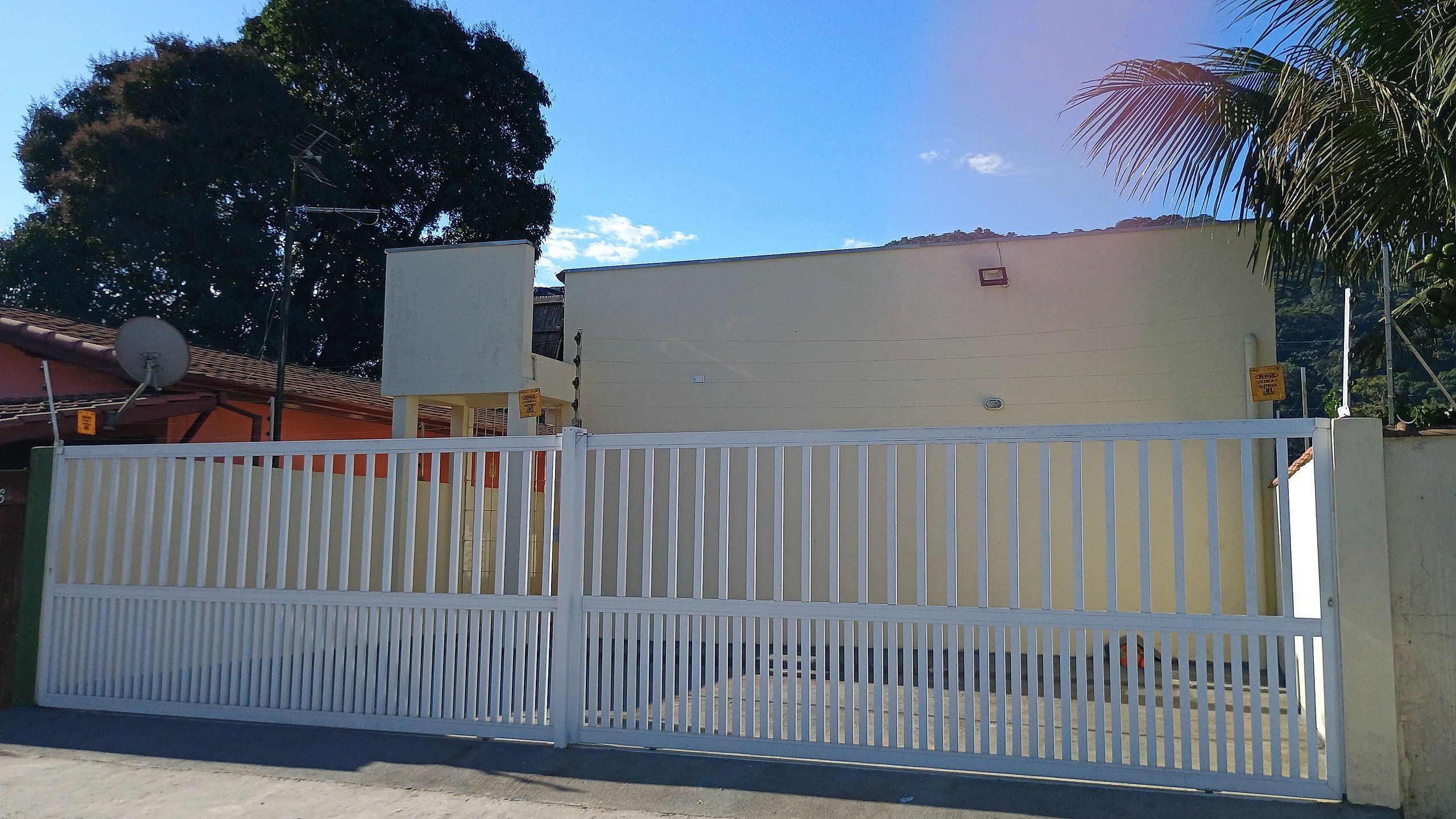 Uma área cercada por um muro branco, um edifício com telhado plano e céu claro.