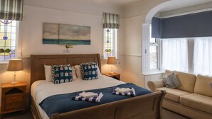 A neatly arranged bedroom with a bed, bedside tables, a sofa, and a painting on the wall. - South Bay Beach House (Bridlington)