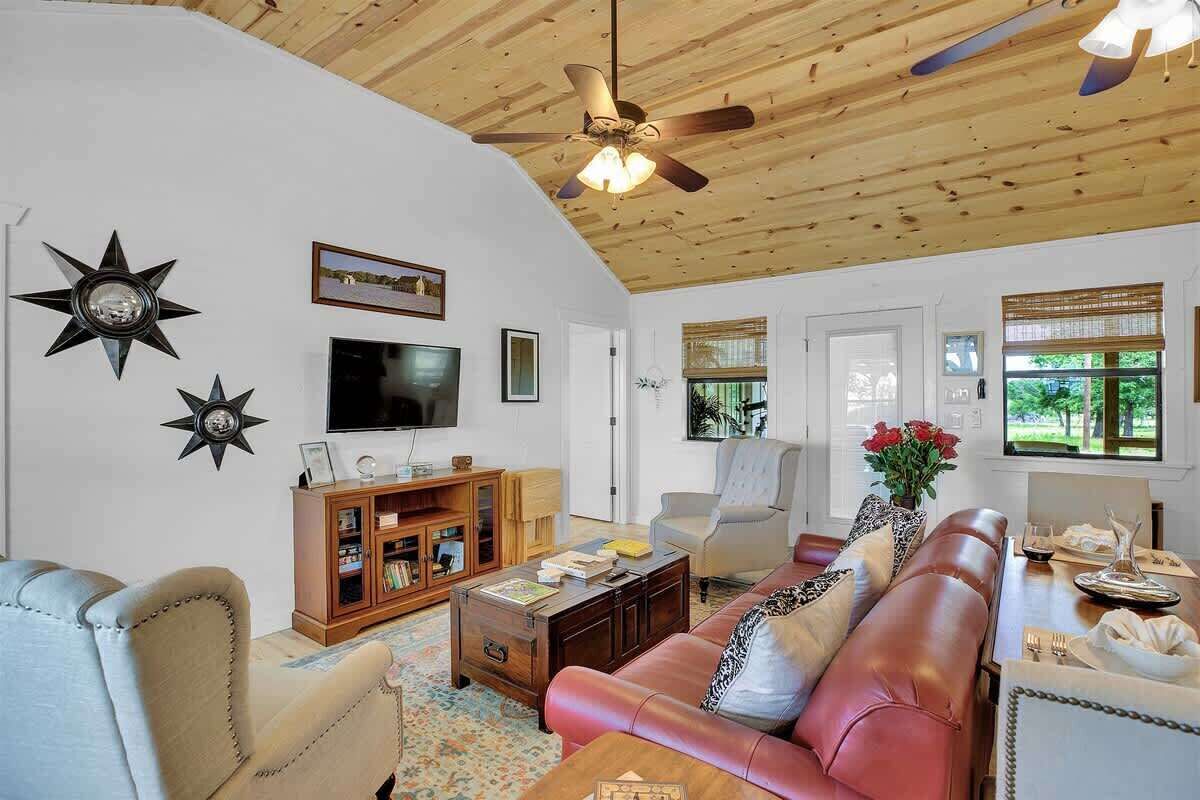 A living room with a wooden ceiling, a ceiling fan, a TV, a bookshelf, a sofa, and a dining table with chairs.