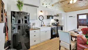 A modern kitchen with white cabinets, a black refrigerator, and a dining area with a leather chair and a table set for two. - Luxurious Cottage on 3-acre's in Fred Wine Country (Fredericksburg)