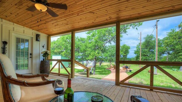 A covered outdoor seating area with a wooden deck, a glass table, and a chair. - Luxurious Cottage on 3-acre's in Fred Wine Country (Fredericksburg)
