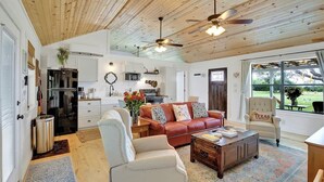 A spacious living room with a wooden ceiling, a leather sofa, a white armchair, and a coffee table. - Luxurious Cottage on 3-acre's in Fred Wine Country (Fredericksburg)