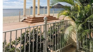 En overdækket pavillon med kuppel, beliggende tæt på en strand med klart himmel og palmer.